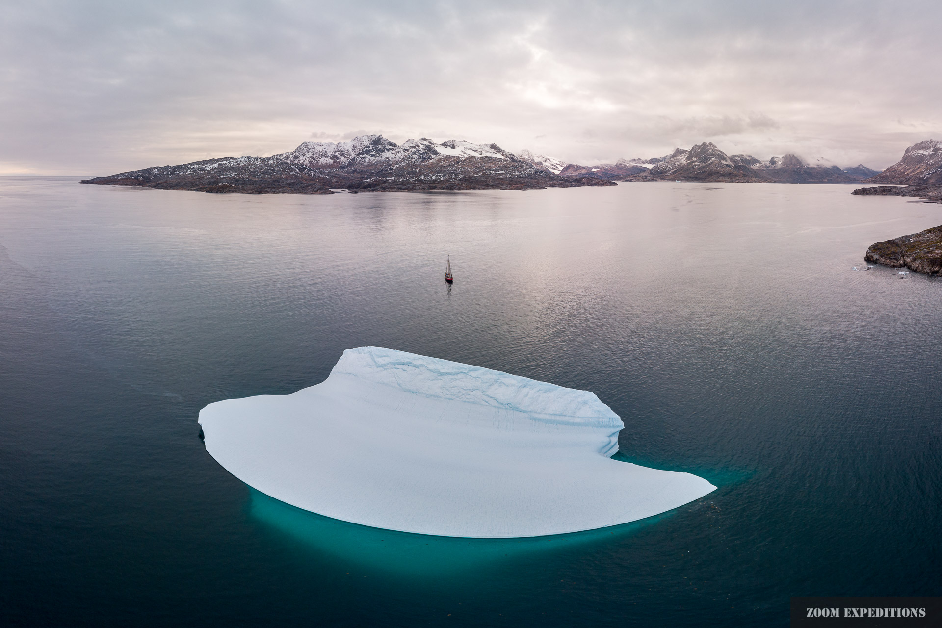 Das Expeditionsschiff Arktika in Ostgrönland hinter einem mächtigen Eisberg