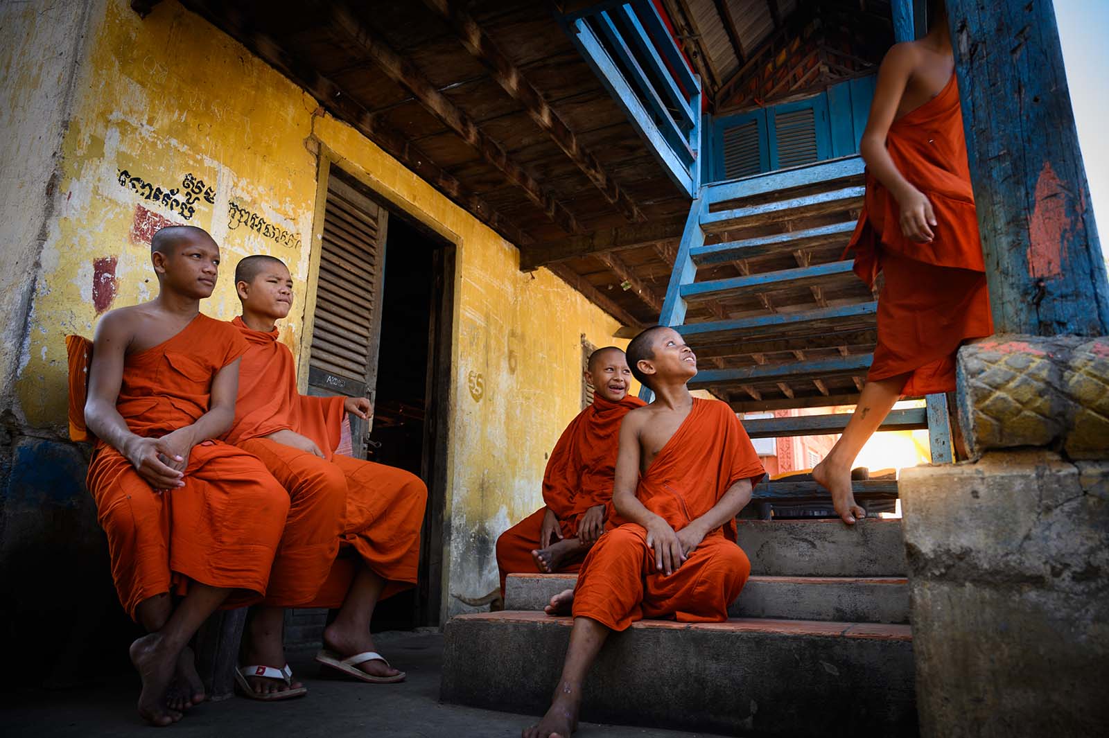Buddhistische Novizen in orangefarbenen Roben begegnen sich vor einem farbenfrohen Klostergebäude in Kambodscha.