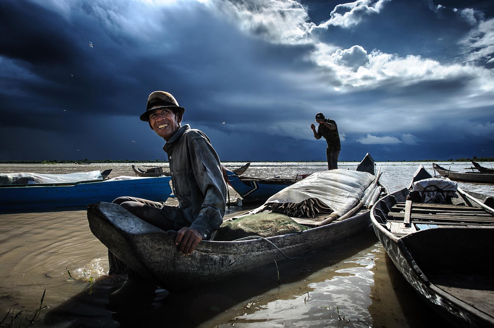 Kambodschanische Fischer in traditionellen Holzbooten auf dem Tonle Sap unter eindrucksvollen, aufziehenden Gewitterwolken.